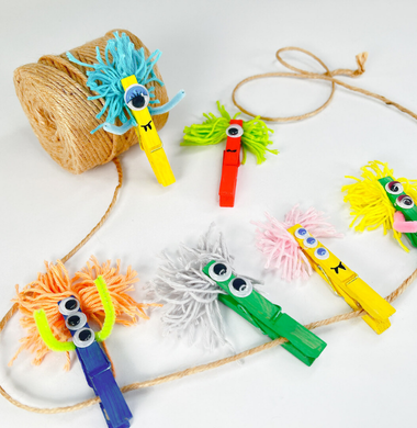 Wäscheklammermonster, gebastelt aus bunten Wäscheklammern, Wackelauge, Armen aus Pfeifenputzern und Haaren aus Wolle.