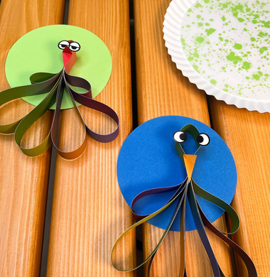 Aus dünnen Papierstreifen gebastelte Vögel, die auf winem Holztisch liegen.