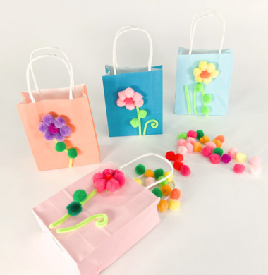 Mehrere Papiertaschen, die mit Pompons geschmückt sind. Die Pompons stellen eine Blume dar.