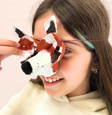 Ein Mädchen trägt eine Tiermaske aus einer bemalten Eierkartonschale.