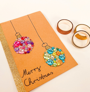 Gebastelte Weihnachtskarte aus braunem Kraftpapier, verziert mit Glitzersteinen in Form von Weihnachtskugeln.