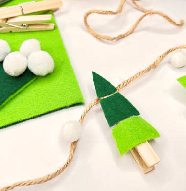 Weihnachtsbaum-Girlande. Kleine Weihnachtsbäume ausgeschnitten aus Bastelfilz und aufgeklebt auf Wäscheklammern, die an einem Jutegarn geklemmt wurden.