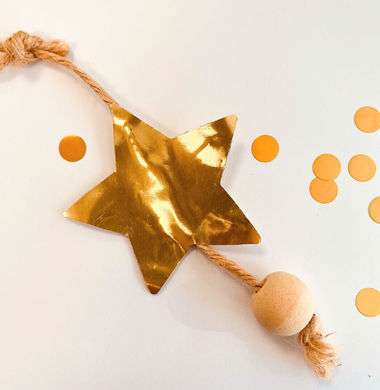 Ein Stern aus goldener Folie, das auf eine Jute-Kordel geklebt wurde und mit einer Holzperle geschmückt wurde.