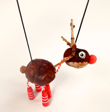 Rentier aus zwei Kastanien, die mit Wolle verbunden sind. Die Hufen sind aus langen Holzperlen, das Gesicht besteht aus Wackelaugen und einer Pomponnase. Das Gewei ist aus kleinen Ästen. Die Figur hängt an zwei Schnüren.