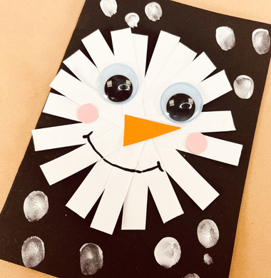Eine gebastelte Weihnachtskarte aus Fotokarton. Verziert mit Papierstreifen, die im Kreis auf die Karte geklebt wurden und mit Wackelaugen und einem Marker sowie einem orangenen Dreieck als Nase verziert wurde, sodass es aussieht wie ein Schneemanns-Gesicht.