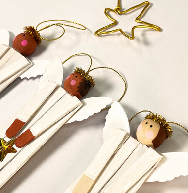 Ein Engel aus Holzstäbchen, mit kleinen Holzflügeln, einem Kopf aus einer Holzperle, einem Heiligenschein aus einem Glitzerpfeifenputzer und einem Glitzerstern.