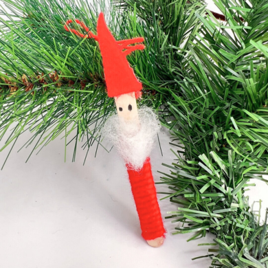 Kleiner gebastelter Weihnachtsmann aus einem Holzstäbchen, das mit roter Wolle umwickelt wurde und mit Watte geschmückt ist.