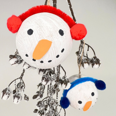 Weiß bemalte Kugeln, die mit Pfeifenputzer und Pompons zu Schneemannsköpfen geschmückt wurden.