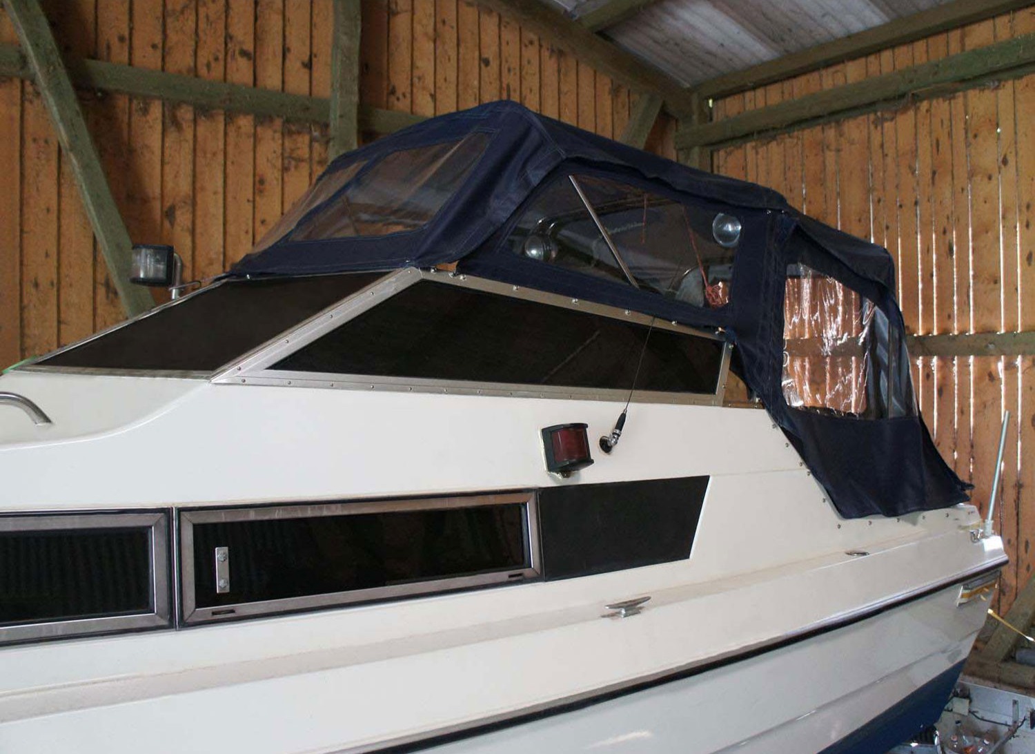 Maßgefertigte Bootsabdeckung aus dunkelblauem Planenmaterial auf einem Motorboot in einer Halle.