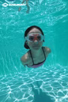 Ein Mädchen trägt die Schildkröt Junior Schwimmbrille Bali 4+ rot beim Schwimmen unter Wasser in einem klaren blauen Pool. Sonnenlichtmuster tanzen auf dem Boden. Das SCHILDKRÖT-Logo erscheint in der oberen linken Ecke. Inklusive Aufbewahrungstasche.