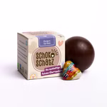 Eine Schachtel SchokoSchatz für Lieblingsmenschen - Ein Herz für Dich steht neben einer runden Schokoladenkugel und einem kleinen herzförmigen Speckstein von SchokoSchatz auf weißem Hintergrund.