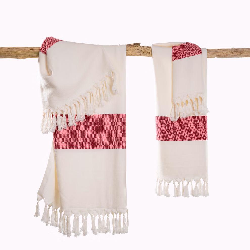 HängemattenGlück Strandtuch aus Bio-Baumwolle zweifarbig in 7 Farbkombinationen _31628 weiß-rot Die zweifarbigen Strandtücher aus Bio-Baumwolle von HängemattenGlück hier in Creme mit roten geometrischen Streifen und Fransen hängen über einer Holzstange vor weißem Hintergrund. weiß-rot