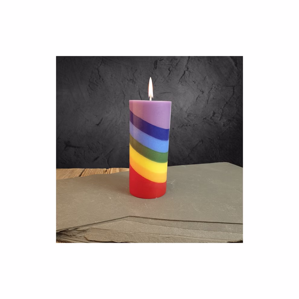 Himalaya Salt Dreams Stumpenkerze multicolor ca. ø 56 x H 125 cm_33491 Die "Stumpenkerze multicolor" von Himalaya Salt Dreams (ca. ø 56 x H 125 cm) zeigt regenbogenfarbene Streifen und steht auf einer grauen Oberfläche vor einem dunkel strukturierten Hintergrund.