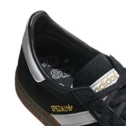 Ein klassischer Sneaker aus schwarzem Wildleder mit weißen Streifen und einer braunen Gummisohle. Der Schuh hat ein schlichtes Design mit einem kleinen goldenen Logo seitlich.