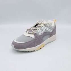 Moderner Sneaker mit grauem Wildleder und Mesh-Obermaterial. Der Schuh hat weiße Akzente und gelbe Details an der Sohle was ihm einen sportlichen und stilvollen Look verleiht.