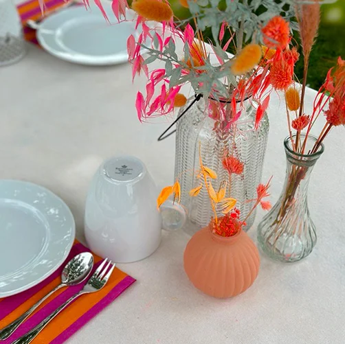 Neonfarbige Trockenblumen und Servietten auf einem gedeckten Tisch