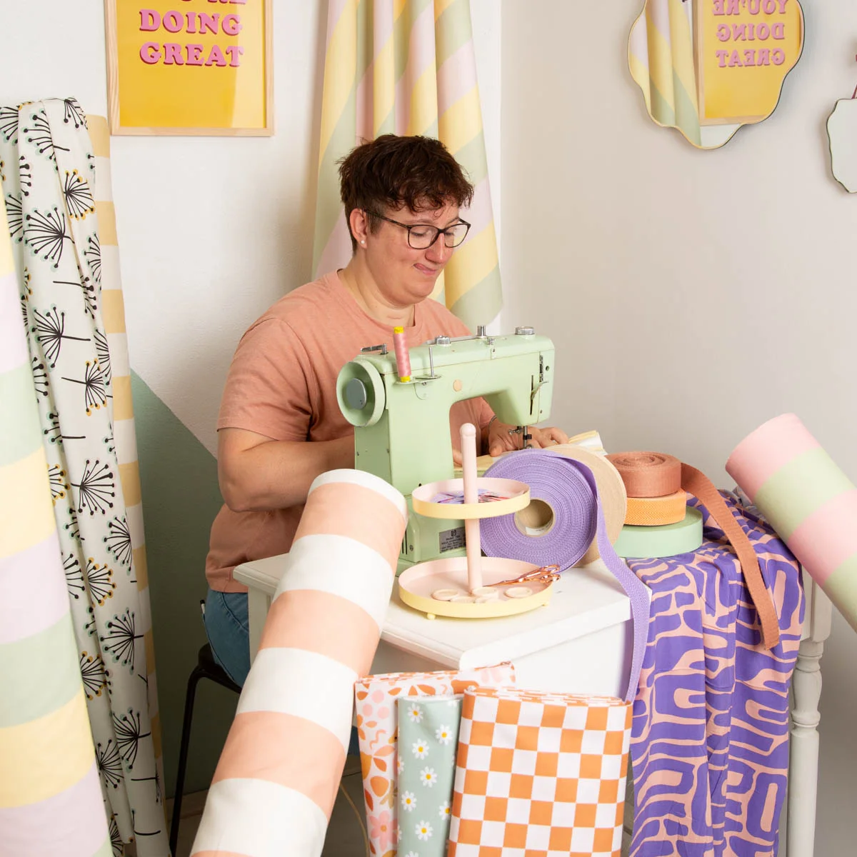Frau näht an der Nähmaschine im bunten Nähzimmer mit farbenfrohen Dekostoffen als Meterware in Retrodesign – kreative Handarbeit mit SCHÖNER LEBEN Stoffen.