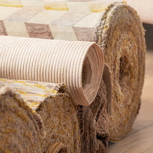 Drei aufgerollte Stoffballen mit unterschiedlichen Polsterstoffen in warmen Beige- und Gelbtönen. Im Vordergrund ein Rippstoff in Beige, daneben Stoffe mit geometrischem Muster und