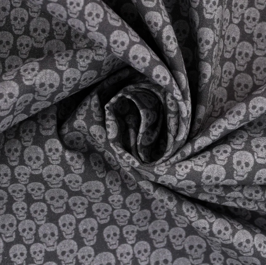 toff mit dichtem Muster aus kleinen Totenköpfen in Hellgrau auf schwarzem Hintergrund. Der Stoff ist kunstvoll zu einer Spirale gelegt.