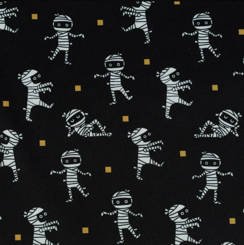 Schwarzer Stoff mit weiß illustrierten Mumienfiguren in verschiedenen Positionen, vereinzelt ergänzt durch kleine gelbe Quadrat