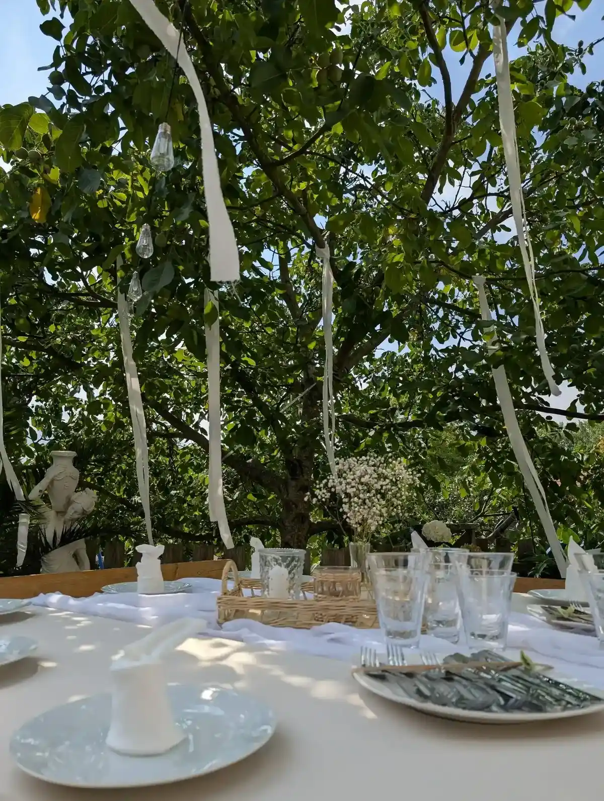 Weiße Deko im Garten – gedeckter Tisch mit Stoffbahnen, Schleierkraut in Glasvase und Windlichtern.