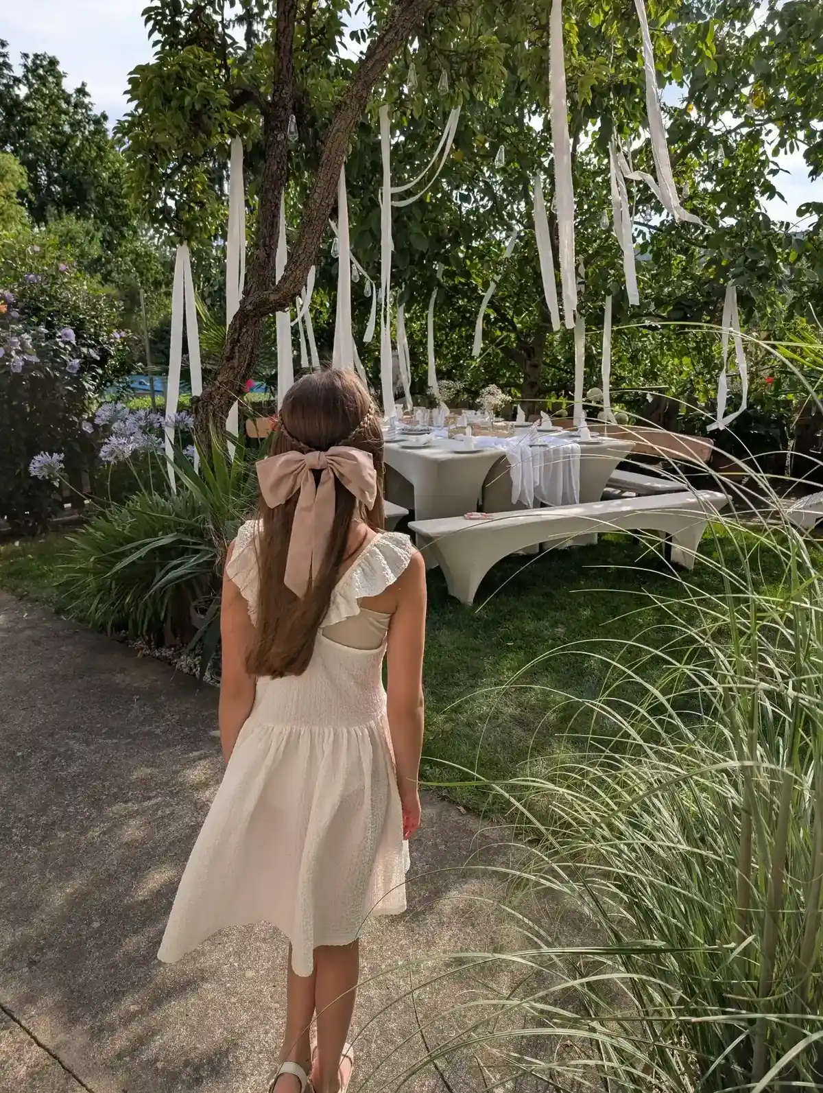 Mädchen im weißen Kleid mit Schleife im Haar vor einer festlich gedeckten Tafel, romantische Deko in Weiß.