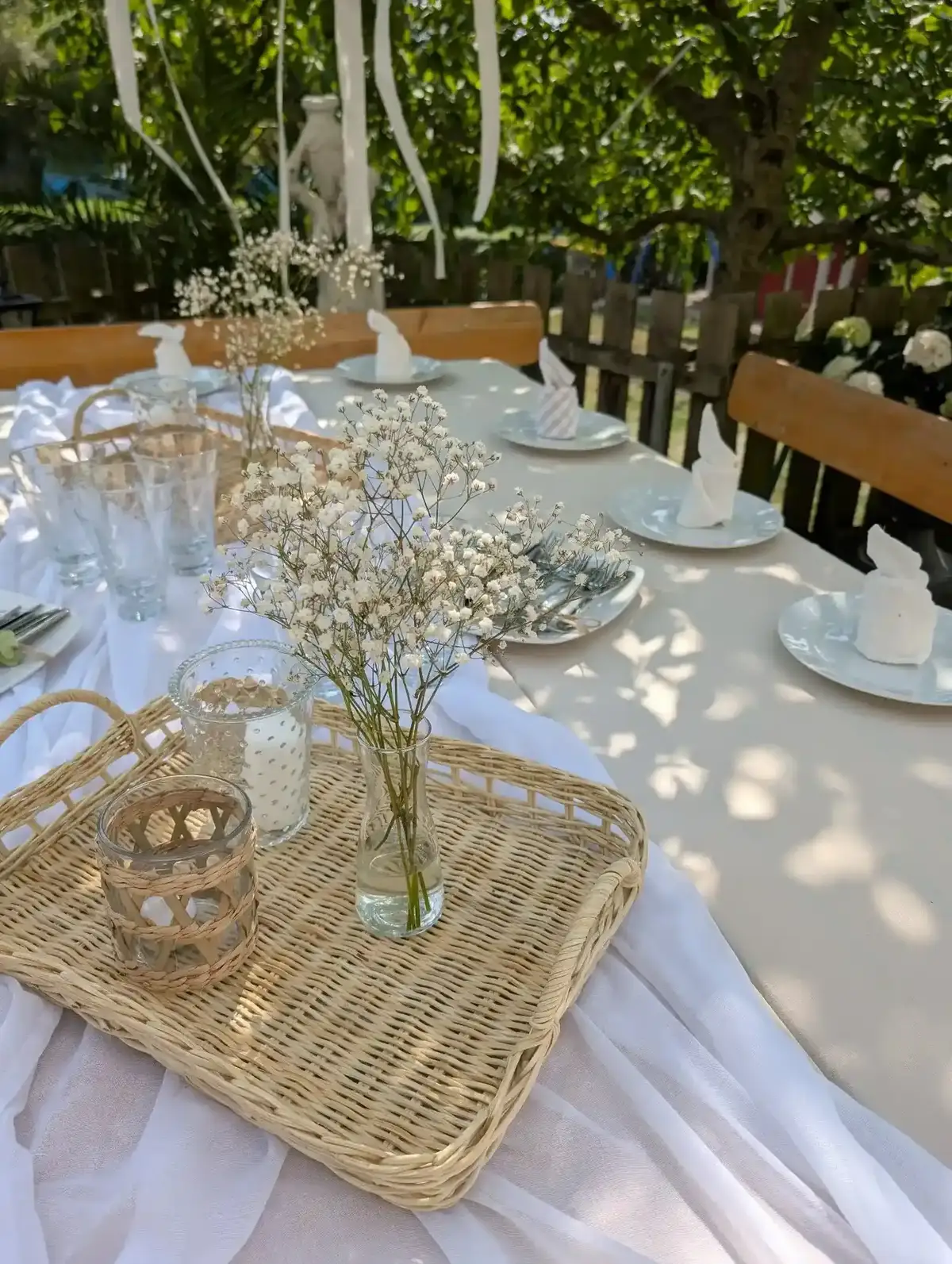 Weiße Deko – Tisch mit Rattan-Tablett, Glaswindlichtern und gefalteten Stoffservietten.
