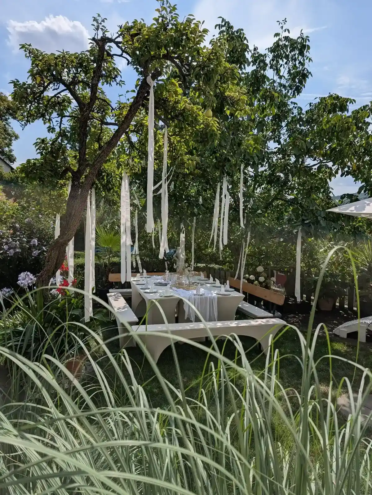 Weiße Deko im Garten – gedeckter Tisch mit Stoffbahnen, Schleierkraut in Glasvase und Windlichtern.