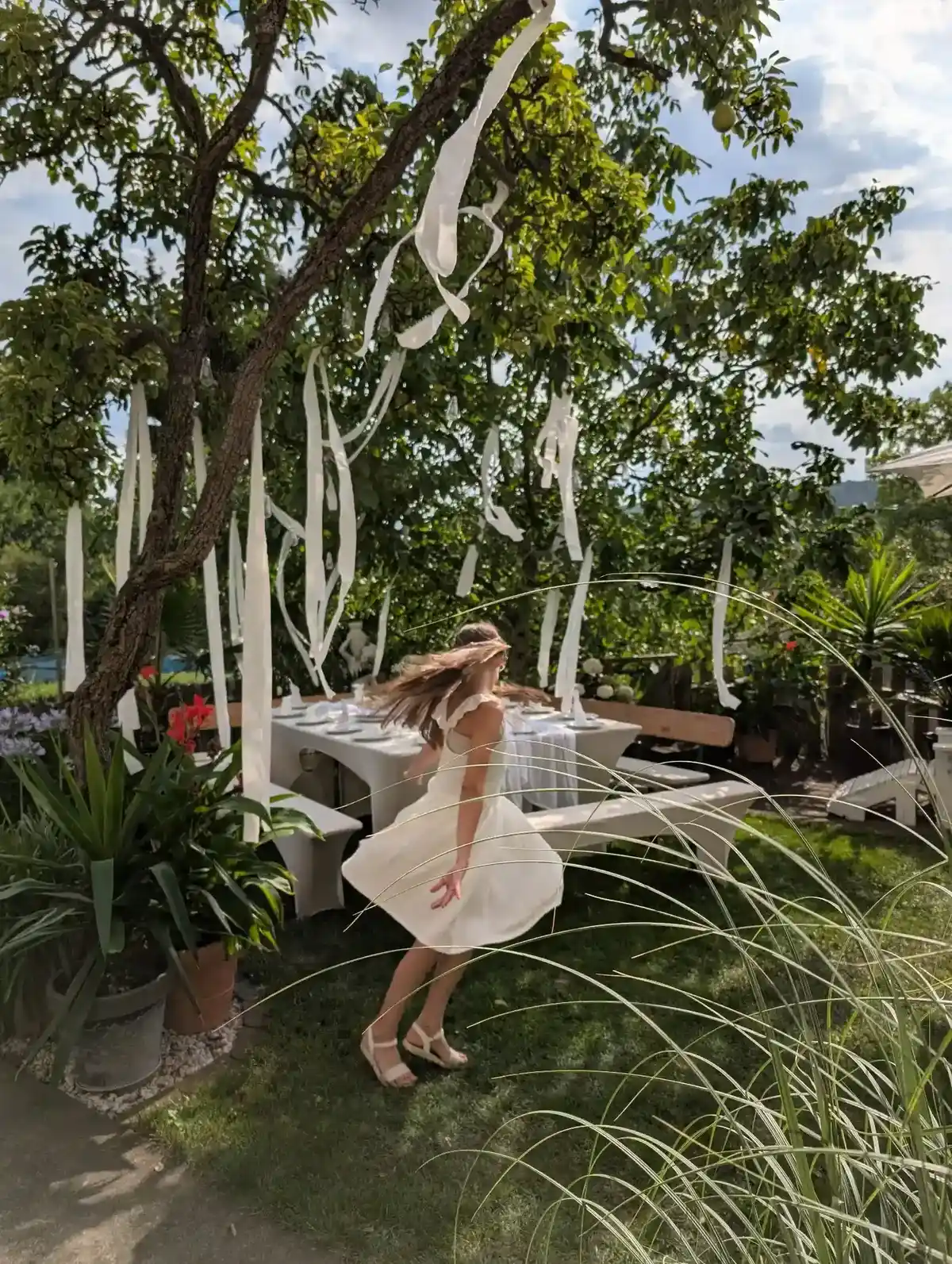 Sommerparty in Weiß – Mädchen tanzt im weißen Kleid vor einer festlich dekorierten Garten-Tafel.