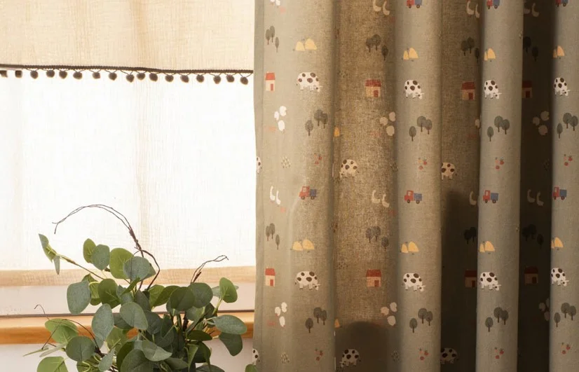 Ausgefallene Gardinen im Landhausstil für das Kinderzimmer – blickdichter Vorhang mit Bauernhof-Motiv in Grün und beiger Raffrollo mit Bommeln. Perfekte Fensterdekoration für ein natürliches Ambiente.