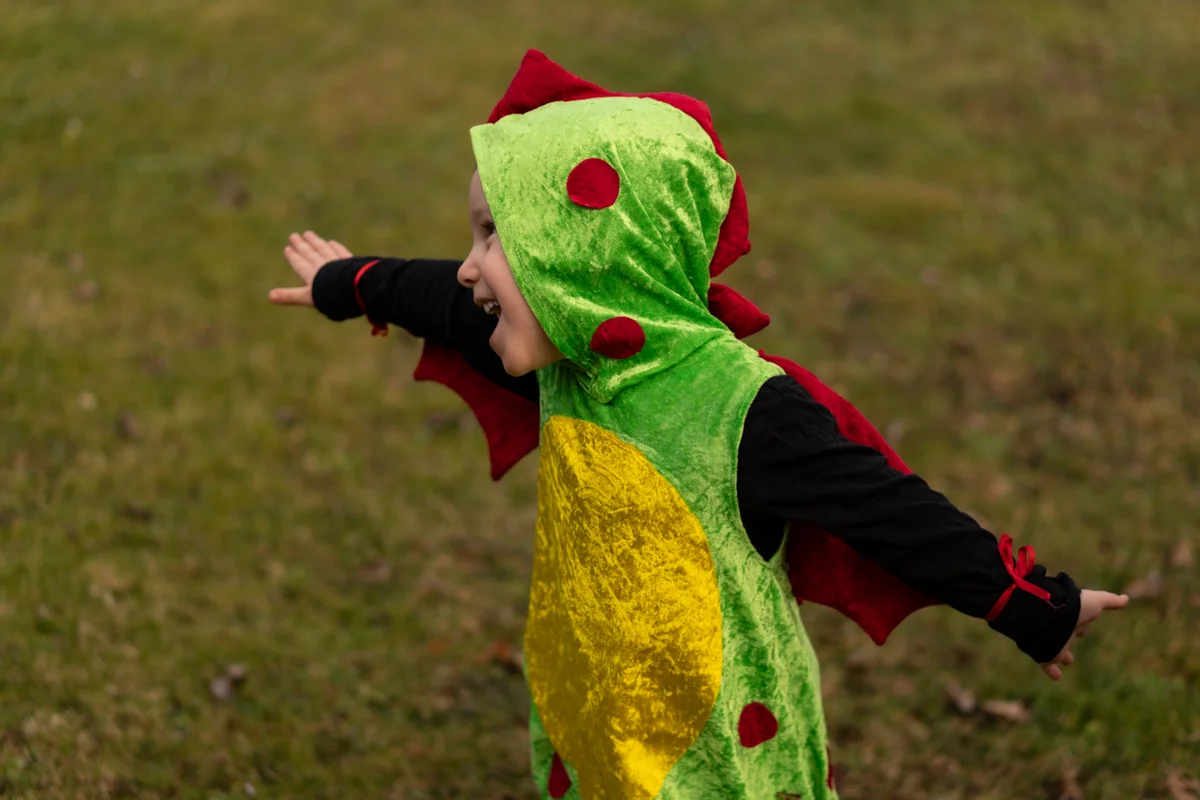 Lachendes Kind im grün-roten Drachenkostüm aus Faschingsstoff, ausdrucksstark mit Flügeln und Punkten – perfekt für Karneval Lachendes Kind im grün-roten Drachenkostüm aus Faschingsstoff, ausdrucksstark mit Flügeln und Punkten – perfekt für Karneval