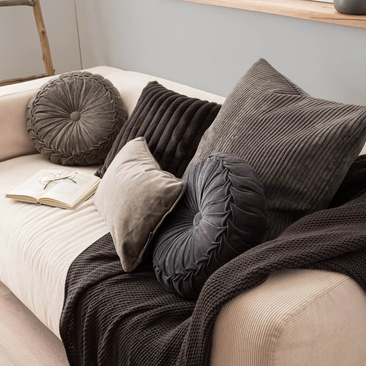 Graue Kissen in verschiedenen Formen und Strukturen auf einem hellen Sofa