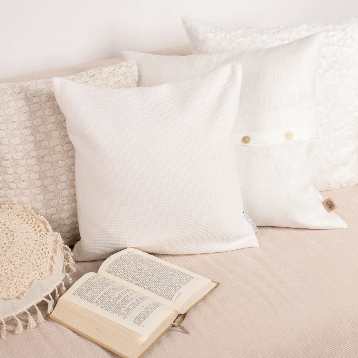 Kissen in weiß auf einer beigen Couch auf der ein Buch liegt
