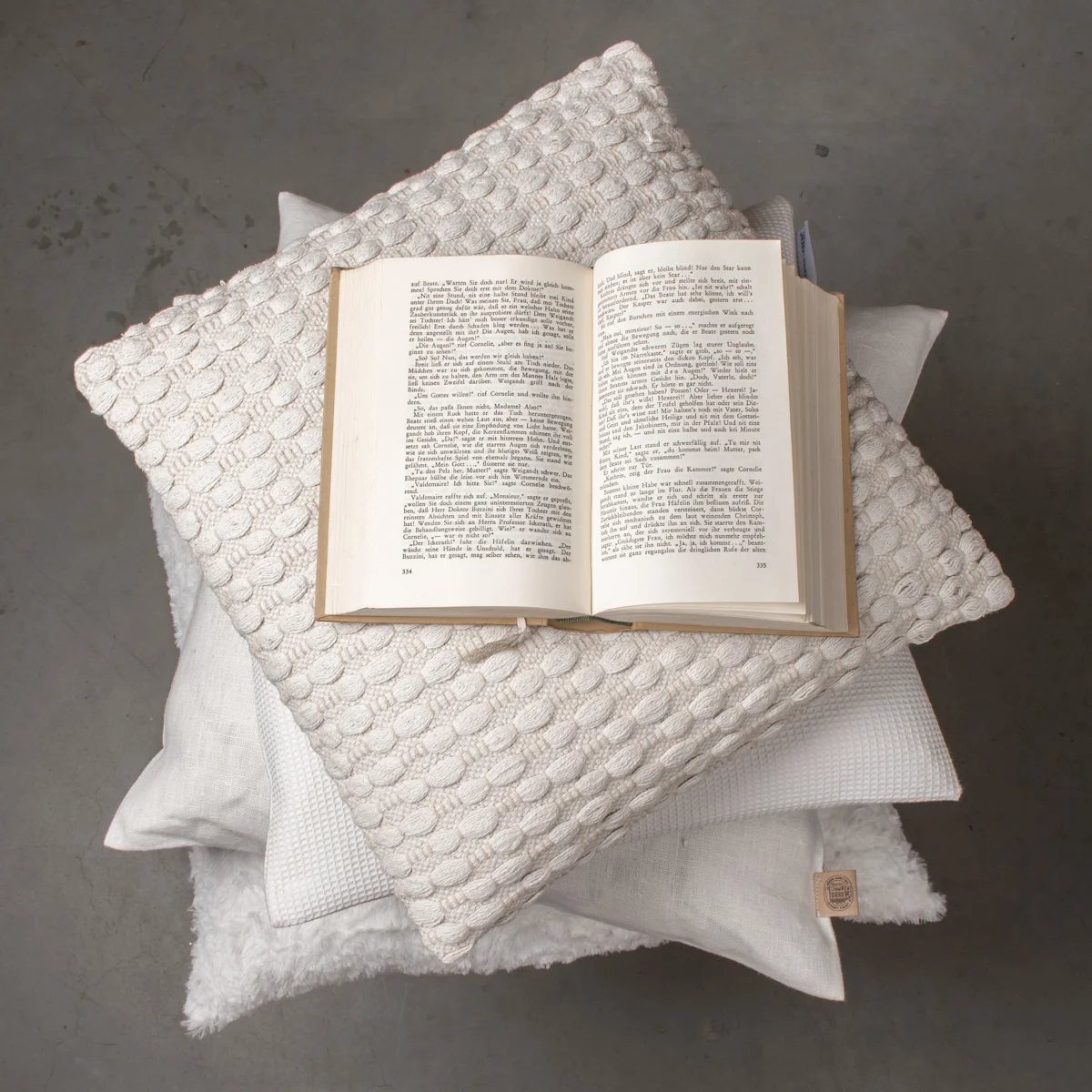Kissenstapel in weiß auf dem ein Buch liegt