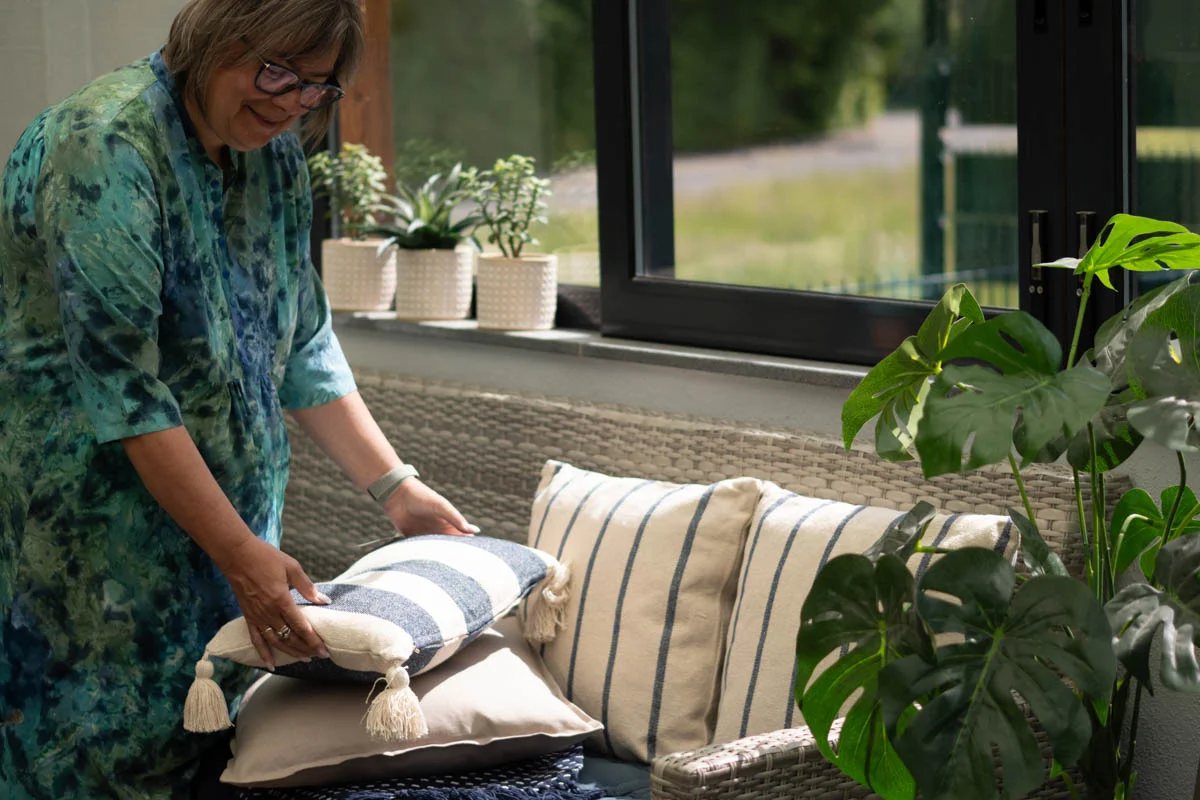 Frau arrangiert dekorative Kissen auf einem gemütlichen Sofa – stilvolle Wohnideen zum Kissen kaufen bei SCHÖNER LEBEN
