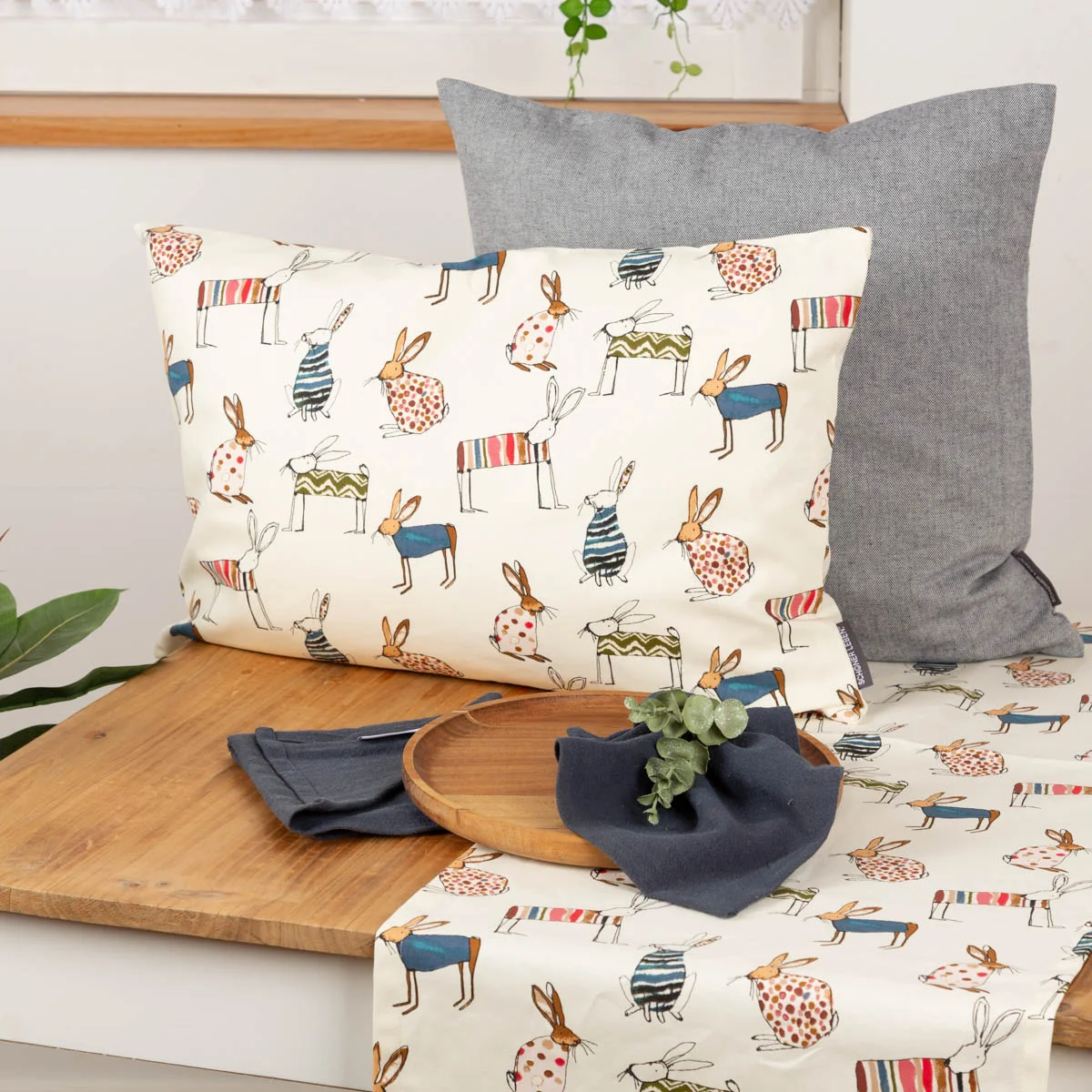 Kissen mit Hasenmotiv und passender Tischläufer als Osterdeko auf Holztisch, dekoriert mit Holztablett Kissen mit Hasenmotiv und passender Tischläufer als Osterdeko auf Holztisch, dekoriert mit Holztablett