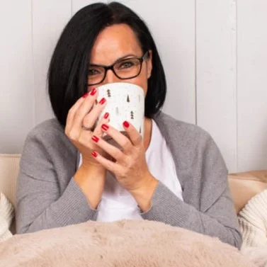 Frau sitzt auf dem Sofa und trinkt aus einer Tasse, die ein schönes Geschenk ist