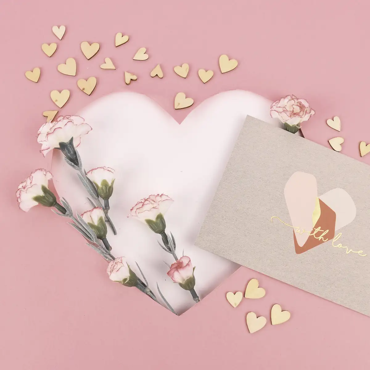 Hochzeitskarte vor einem rosafarbigen Hintergrund, der mit kleinen Holzherzen und Kunstblumen dekoriert ist