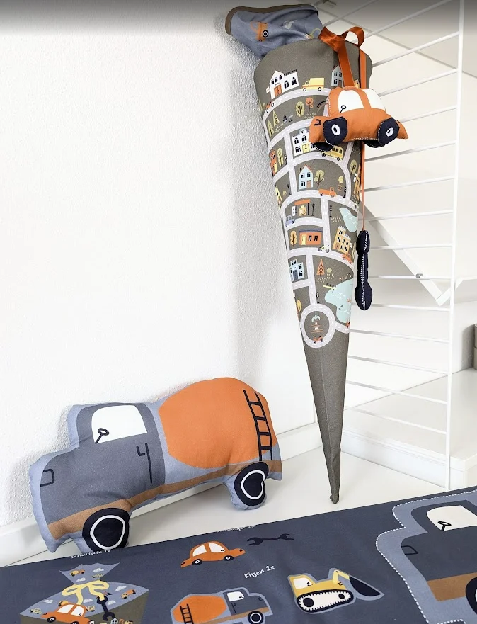 Schultüte mit Straßenszenen und Fahrzeugmotiven, passend  zur Einschulung – dekoriert mit Plüschauto und passendem Kissen im Fahrzeugdesign