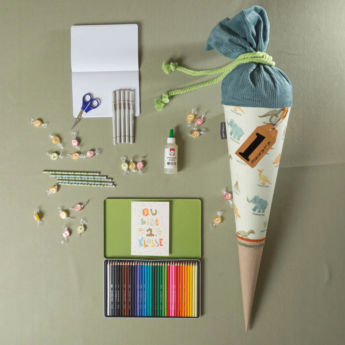 Schultüte mit Dino-Motiv für Jungen, gefüllt mit Buntstiften, ABC-Bonbons, Bastelkleber, Schere, Stiften, Heft und Karte – kreative Geschenkideen zum Schulanfang