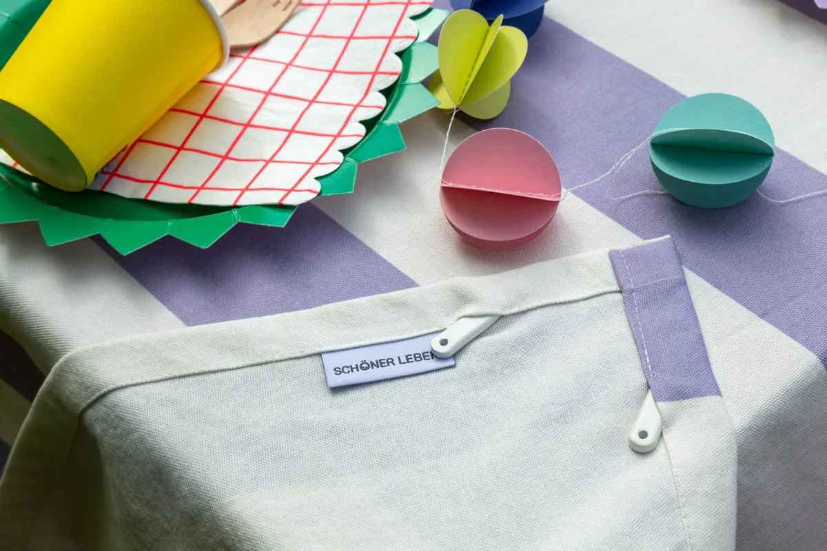Gestreifte Tischdecke in Lila-Weiß mit SCHÖNER LEBEN Label und unauffälliger Bleistäbchen-Beschwerung gegen Wind – Alternative zu Tischdeckenklammern – SCHÖNER LEBEN