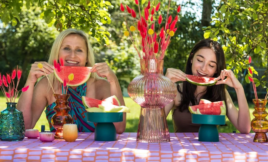 eine Szene im Garten mit zwei Frauen, die an einem festlich gedeckten Tisch im Garten sitzen