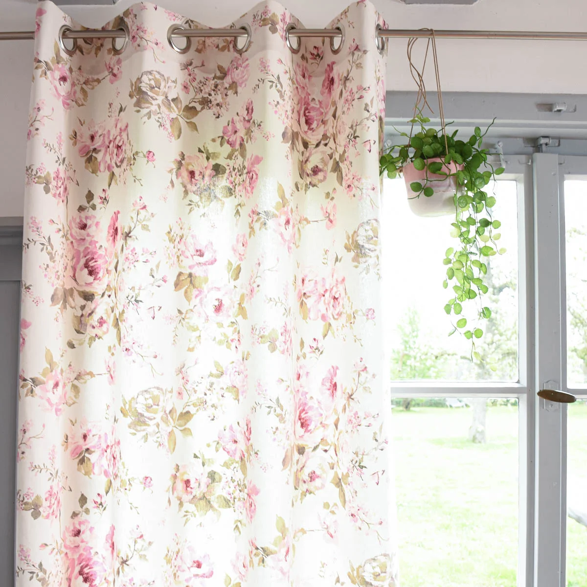 Cremefarbener Ösenschal mit rosa Rosen hängt am Fenster