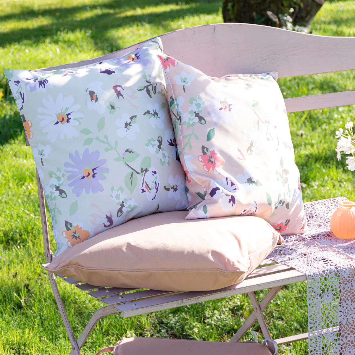 Outdoorkissen in zarten Pastelltönen mit Blumenmuster auf einer rosafarbenen Gartenbank Outdoorkissen in zarten Pastelltönen mit Blumenmuster auf einer rosafarbenen Gartenbank