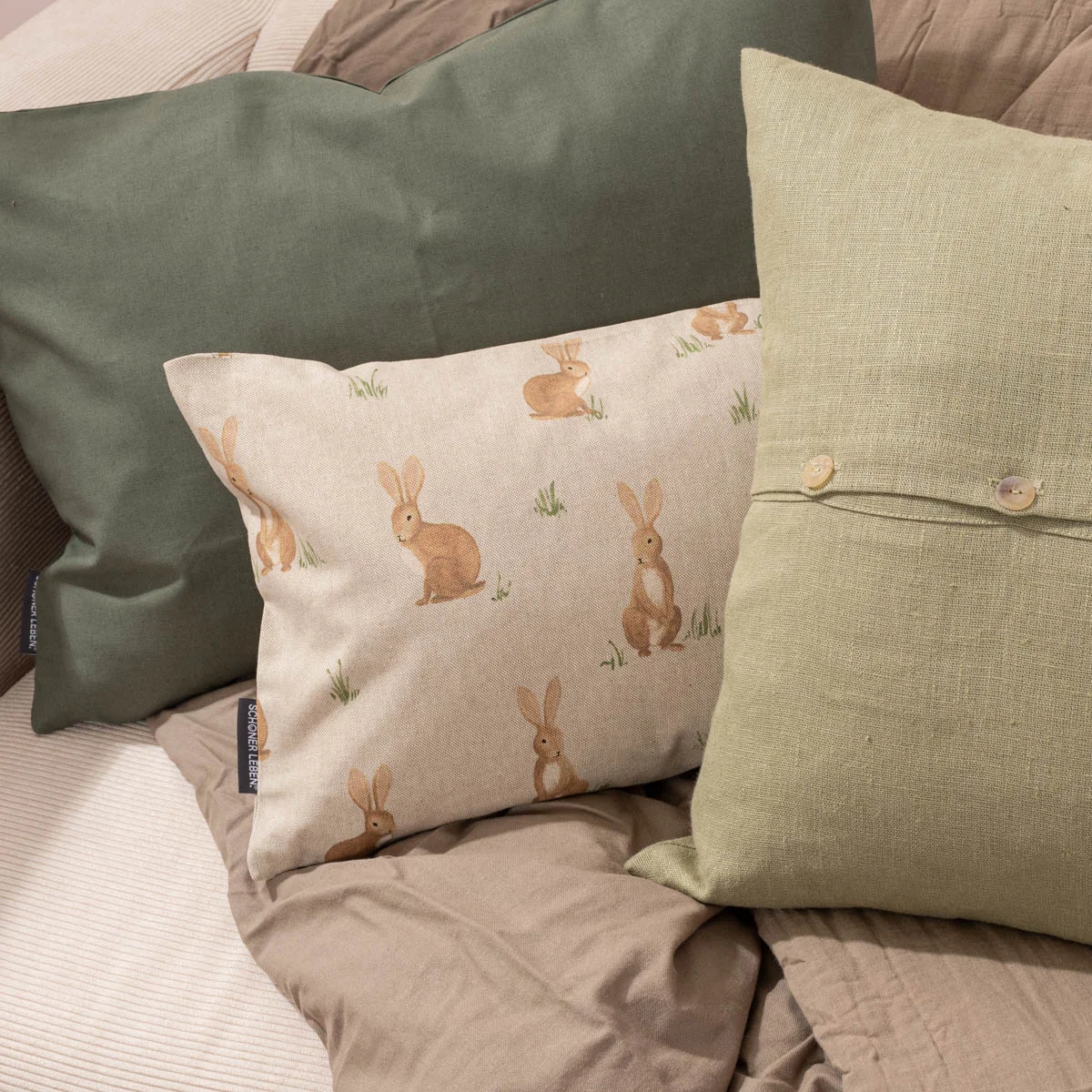 dunkelgrünes, hellgrünes und Naturfarbenes Kissen mit Hasenmotiv auf einem Sofa