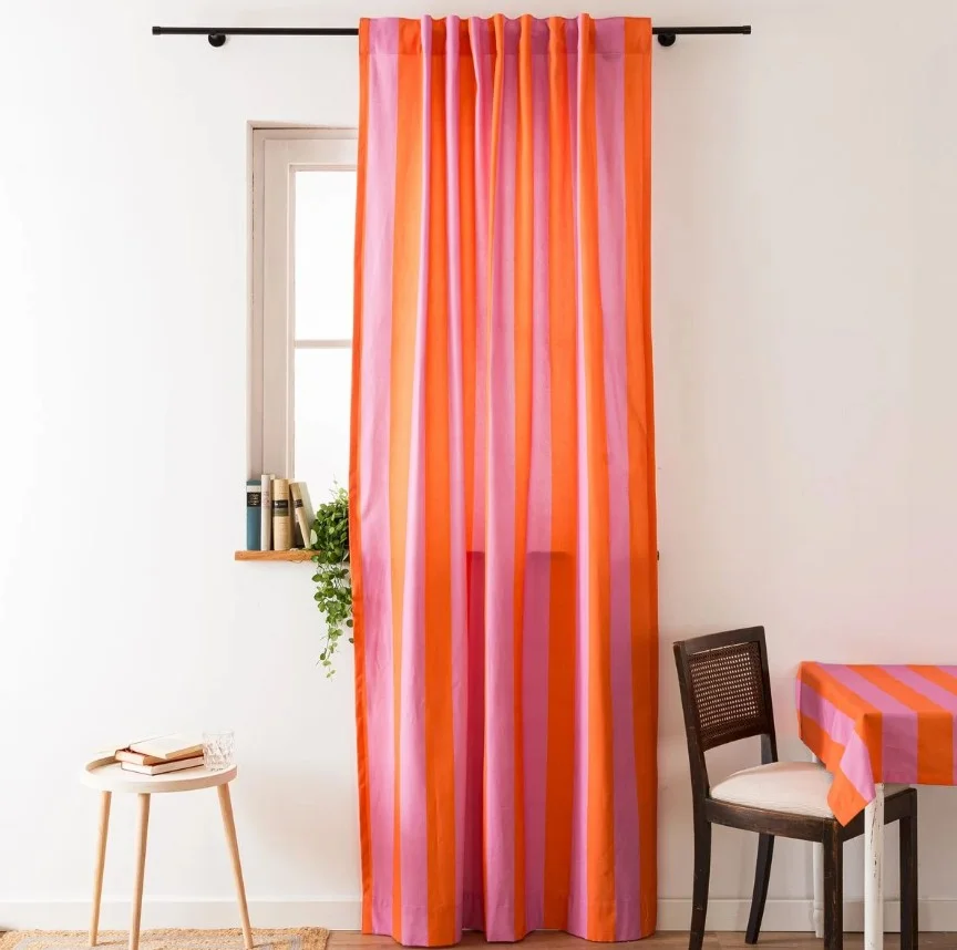 Vorhänge mit breiten orange-pinken Streifen hängen in einem hellen Esszimmer mit passender Tischdecke.