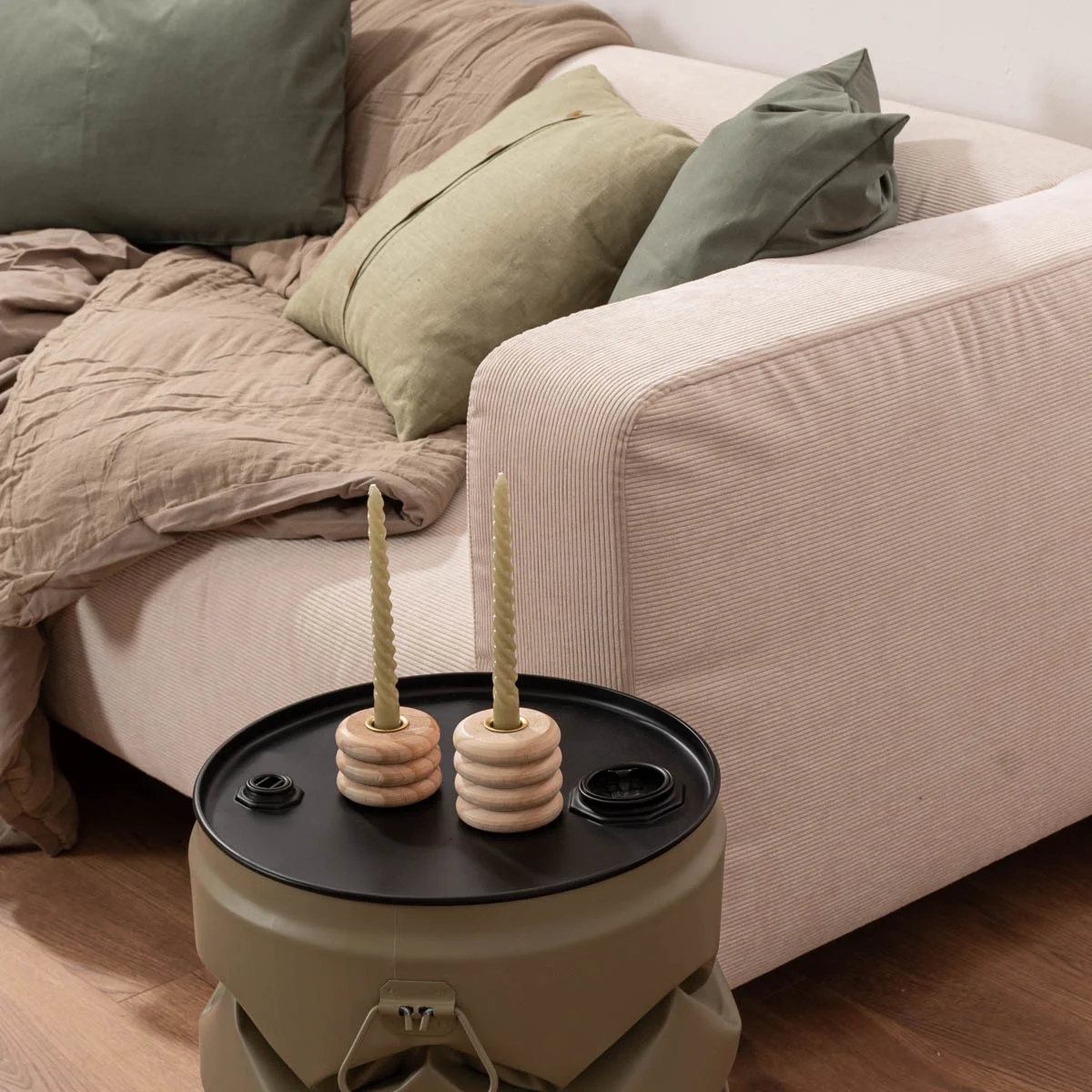 beige Cordsofa mit grünen Kissen vor dem ein Beistelltisch mit 2 Holz-Kerzenhaltern steht