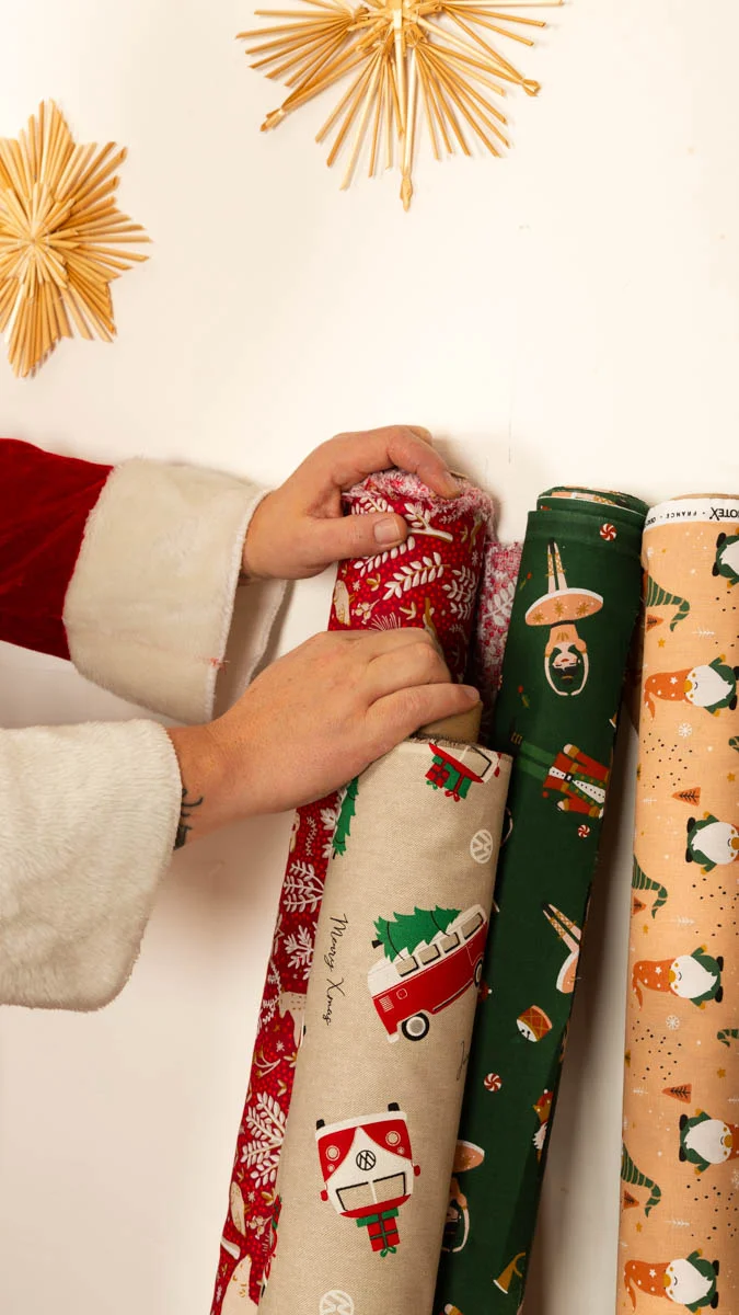 Weihnachtsstoffe als Meterware mit festlichen Motiven: roter Stoff mit Rentieren, beiger Stoff mit einem roten VW-Bus und Tannenbaum, grüner Stoff mit Figuren und orangefarbener St Weihnachtsstoffe als Meterware mit festlichen Motiven: roter Stoff mit Rentieren, beiger Stoff mit einem roten VW-Bus und Tannenbaum, grüner Stoff mit Figuren und orangefarbener St
