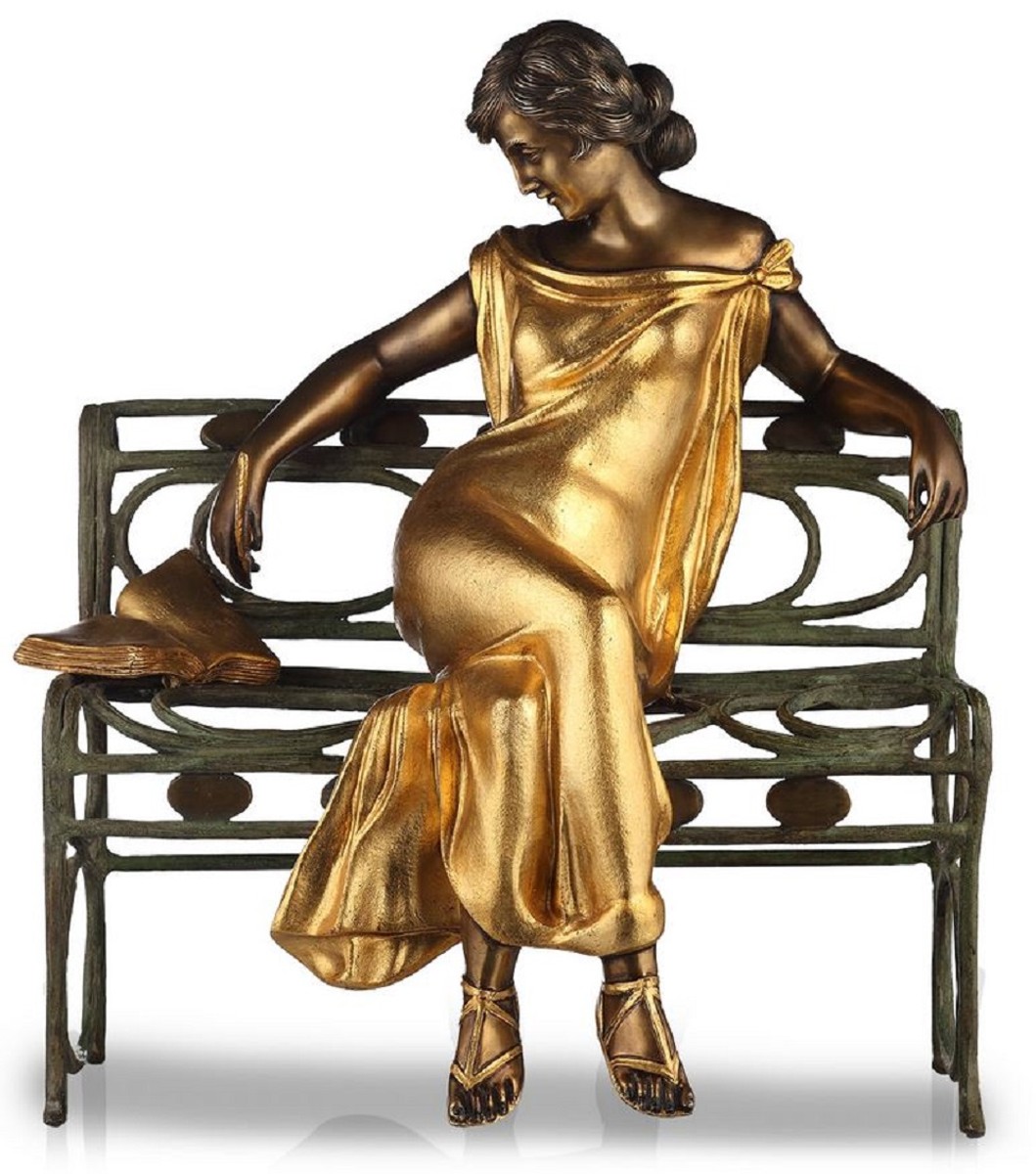 You see an antique bronze figure of a woman in Art Nouveau style sitting on a park bench with an open book next to her. The colors are bronze, gold, partina and black.