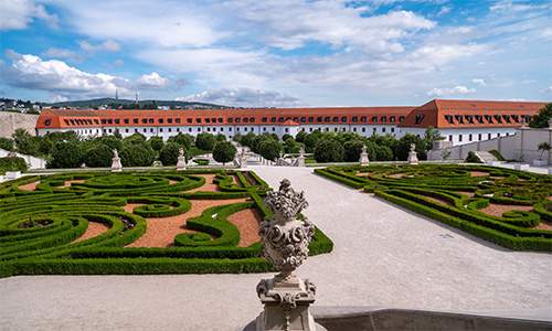 Panorama del jardín del Castillo de Bratislava con una opulenta estatua ornamental de piedra en el centro, rodeada de áreas de vegetación simétrica.